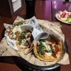 A basket of tacos at Tijuanazo Hipodromo, topped with seasoned meat, onions, cilantro, and creamy sauce.