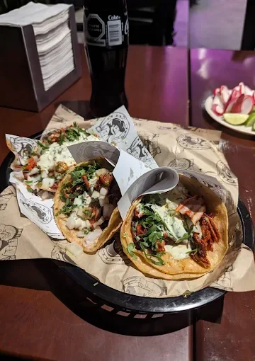 A basket of tacos at Tijuanazo Hipodromo, topped with seasoned meat, onions, cilantro, and creamy sauce.