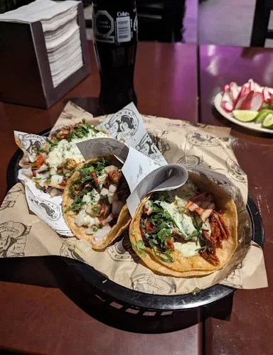 A basket of tacos at Tijuanazo Hipodromo, topped with seasoned meat, onions, cilantro, and creamy sauce.