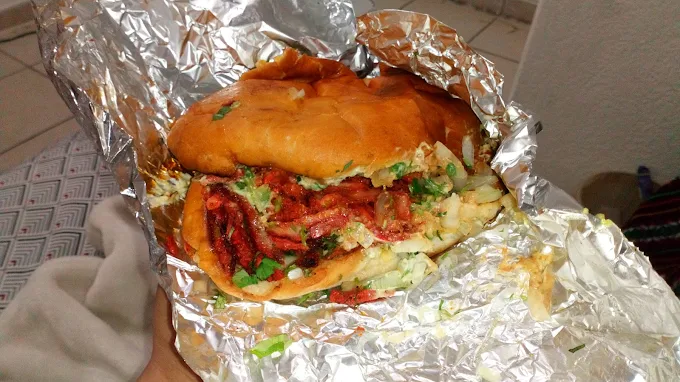 A delicious sandwich at Tijuanazo Hipodromo, loaded with seasoned meat, vegetables, and creamy sauce.