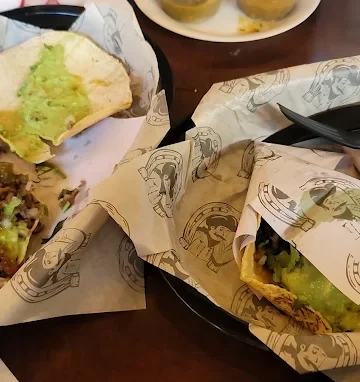 A meal featuring tacos filled with meats and topped with guacamole, served in baskets with additional sides.