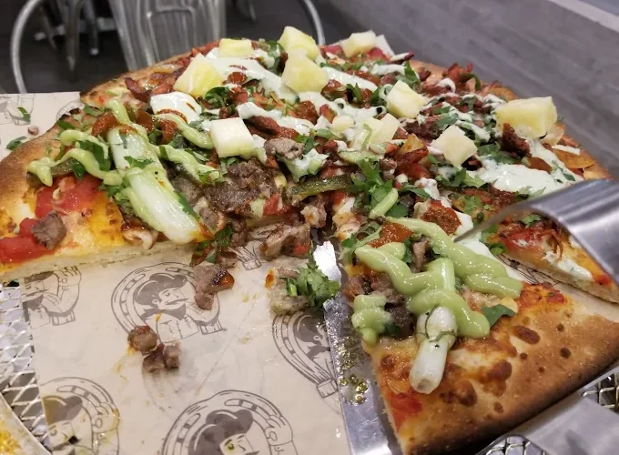 Tasty pizza with various toppings at Tijuanazo Hipodromo, featuring meats and pineapple.