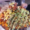 A vibrant, fully loaded pizza with assorted toppings and green sauce at Tijuanazo Hipodromo.