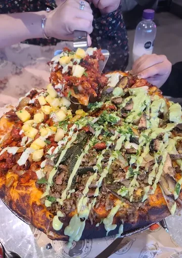A vibrant, fully loaded pizza with assorted toppings and green sauce at Tijuanazo Hipodromo.