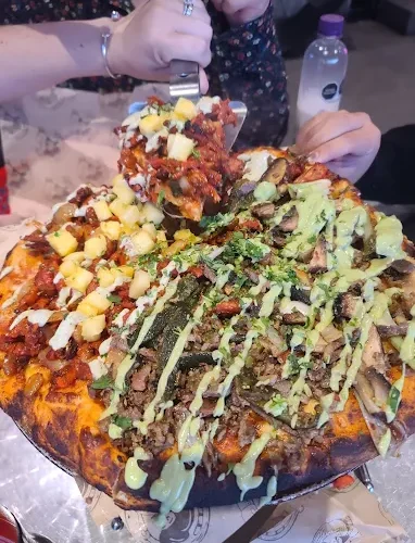 A vibrant, fully loaded pizza with assorted toppings and green sauce at Tijuanazo Hipodromo.