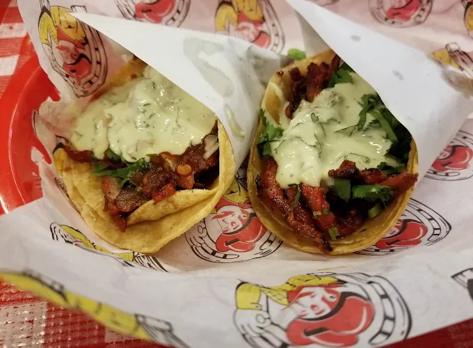 Soft tacos at Tijuanazo Hipodromo, showcasing seasoned meat, herbs, and a creamy topping.