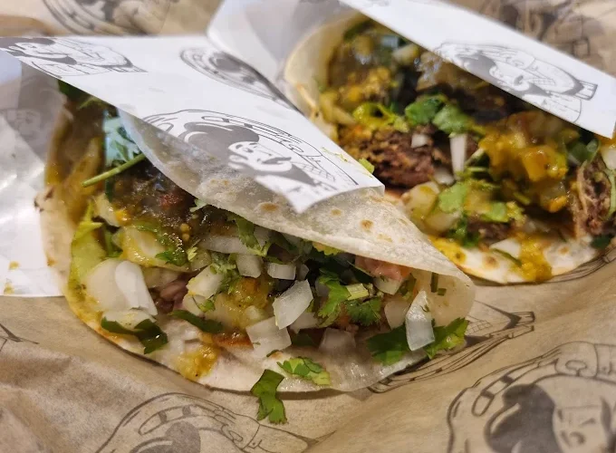 Two flavorful tacos at Tijuanazo Hipodromo, topped with onions, cilantro, and a vibrant salsa.