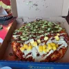 Takeout pizza at Tijuanazo Hipodromo, featuring a mix of toppings including meat and avocado.